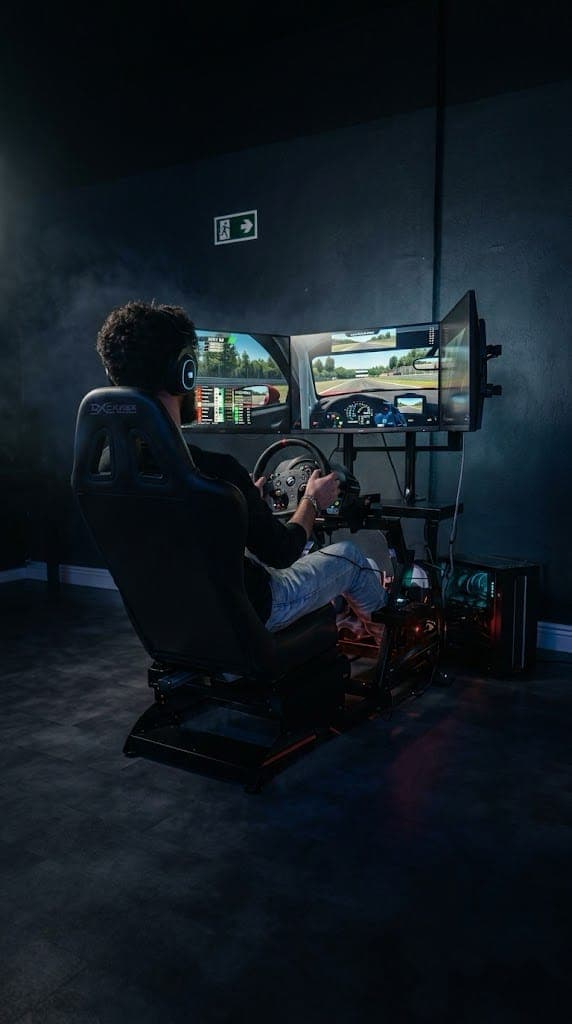 Jogador pilotando no simulador de corrida da GOAT, com volante, pedais, banco concha e três telas